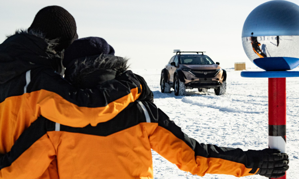 Chris and Julie embracing beside the Ceremonial South Pole, facing the Nissan Expedition Ariya parked in the distance.